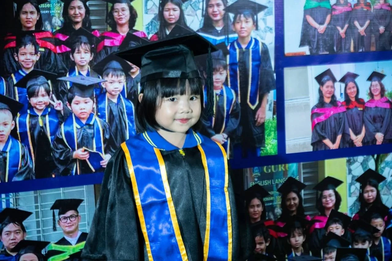 A child in a graduation gown in front of school celebration photographs